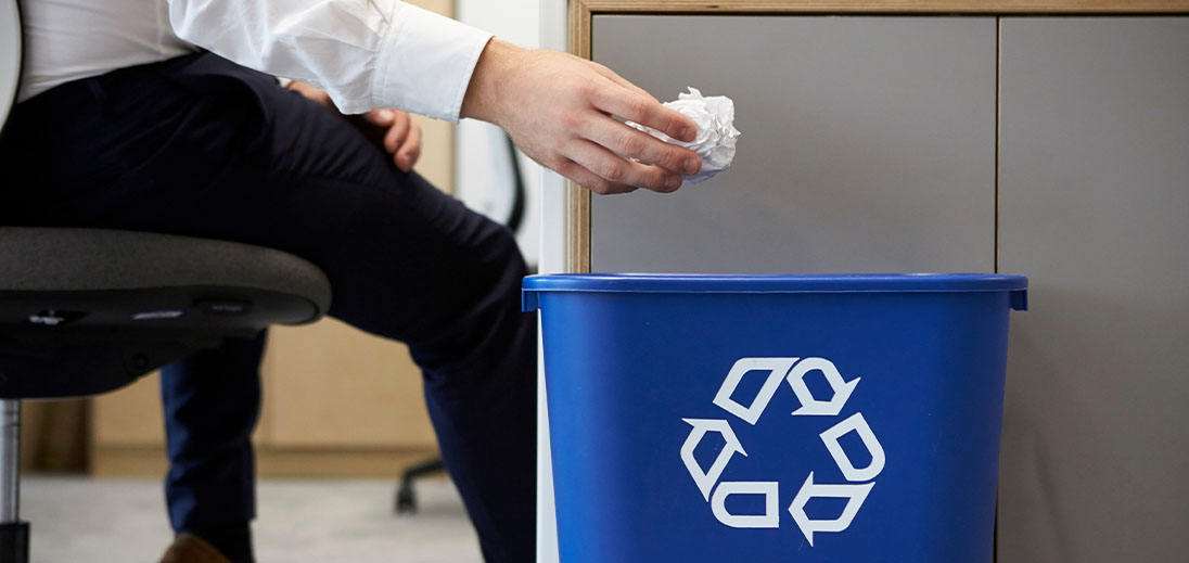 Office worker about to discard a scrunched up piece of paper into a blue recycling bin
