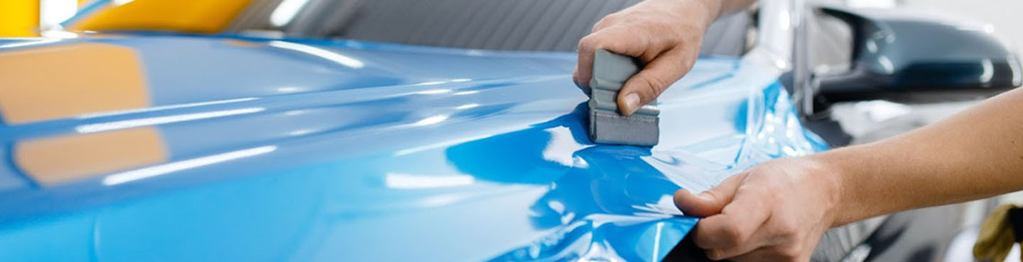 A vehicle detailer applying a blue vinyl wrap to a car