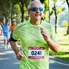 Un homme souriant d'âge moyen, portant un t-shirt vert fluo et des lunettes de soleil, court en plein air avec un dossard de marathon imprimé sur Polyart Laser Soft.
